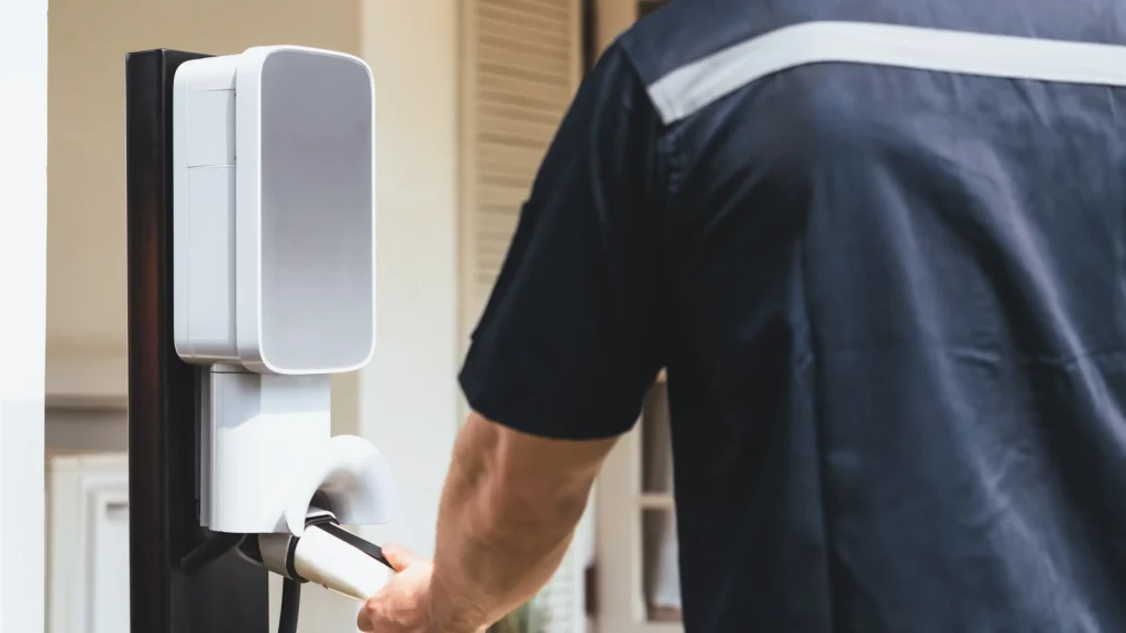 Electrician holding an EV charger plug while installing a wall-mounted home charging station